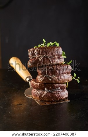 Tasty beef medallions with herbs and threads stacked on spatula against black background