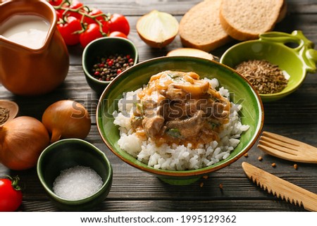 Tasty beef stroganoff and rice in bowl on table
