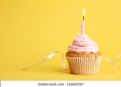 tasty birthday cupcake with candle, on yellow background