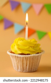 Tasty Birthday Cupcake With Candle On Orange Table Against Party Flags, Closeup