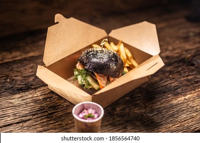 Tasty black burger takeaway in a box of recycled paper on wooden board.