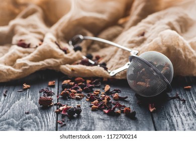 Tasty Black Tea With Dried Fruits, Tea Strainer And Cloth On Wooden Table