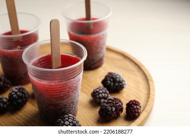 Tasty Blackberry Ice Pops In Plastic Cups On White Wooden Table, Closeup. Fruit Popsicle