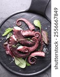 Tasty boiled octopus tentacles, microgreens and salt on grey textured table, top view.