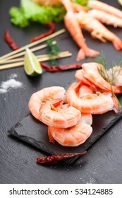 Tasty boiled shrimps with skewers on a stone plate with lime and salad.