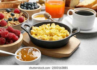 Tasty breakfast. Scrambled eggs, coffee, jam and other food on grey textured table, closeup