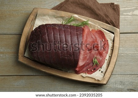 Tasty bresaola, peppercorns and rosemary on wooden table, top view