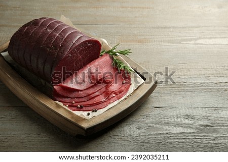 Tasty bresaola, peppercorns and rosemary on wooden table. Space for text