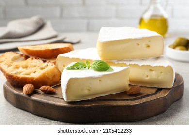 Tasty brie cheese with basil, bread and almonds on wooden board
