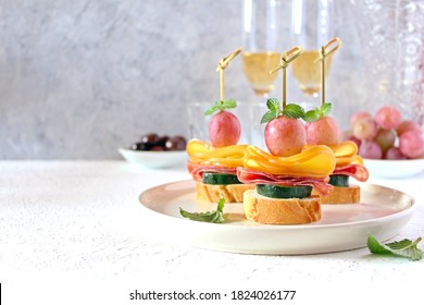 Tasty Canapes With Cucumber, Salami, Cheese And Grapes Served With White Wine. Top View With Copy Space.