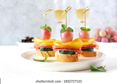 Tasty Canapes With Cucumber, Salami, Cheese And Grapes Served With White Wine. Top View With Copy Space.