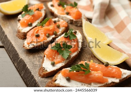 Tasty canapes with salmon, capers, lemon and cream cheese on wooden table, closeup