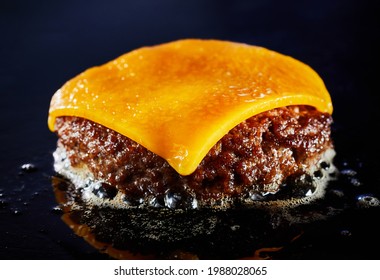 Tasty cheeseburger with beef patty sizzling on a grill in a close up on the melted cheese and juicy meat over a dark background for menu advertising