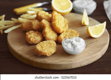 Tasty chicken nuggets with fries, lemon and sauce on cutting board
