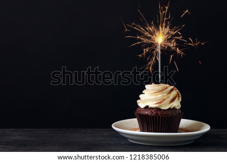 Tasty chocolate cupcake with sparkler on wooden table against dark background