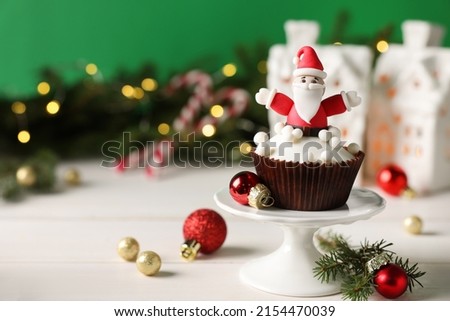 Tasty Christmas cupcake with Santa Claus figure on white table wooden table. Space for text
