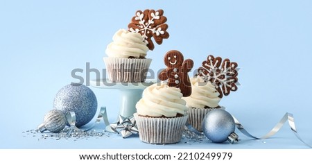 Tasty Christmas cupcakes with gingerbread cookies on light blue background