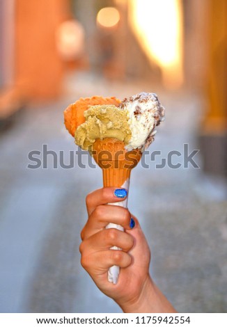 tasty colorful ice cream cone in wafer cup on blured street background taken with hand with blue lacquered nails in Italy