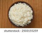 Tasty cooked rice in bowl on bamboo mat, top view