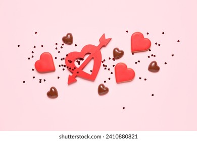 Tasty cookies, chocolate candies and red heart with arrow on pink background. Valentine's Day celebration