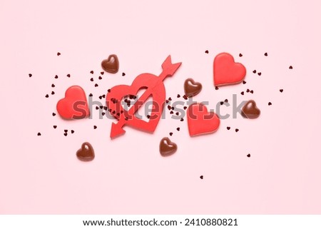 Tasty cookies, chocolate candies and red heart with arrow on pink background. Valentine's Day celebration
