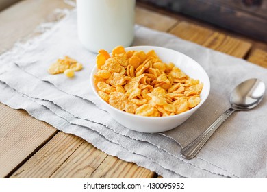 Tasty corn flakes in bowl with bottle of milk. Rustic wooden background with homespun napkin. Healthy crispy breakfast snack. 