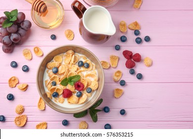 Tasty cornflakes with raspberries and blueberries on pink background