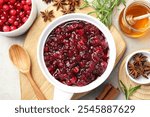 Tasty cranberry sauce in gravy boat, berries, honey and spices on light table, flat lay