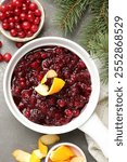 Tasty cranberry sauce in gravy boat, berries, orange peels and fir branches on grey table, flat lay