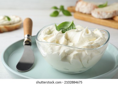 Tasty cream cheese with basil and knife on white wooden table