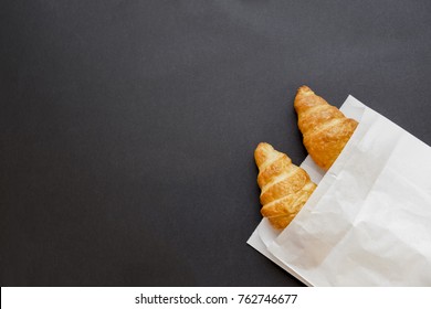 Tasty Croissants In White Paper Bag. Black Background With Sweet Dessert. Top View. Flat Lay. Copy Space For Text