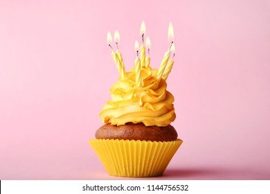 Tasty cupcake with candles on pink background