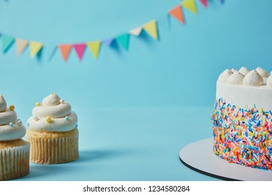 Tasty cupcakes and cake on blue background with bunting