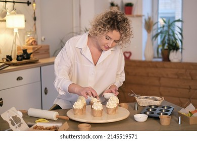Tasty cupcakes on wooden board. Decorating a white cake with cream from the pastry bag. process of decorating cupcakes with white whipped cream. Decorating a white cake with cream from the pastry bag.