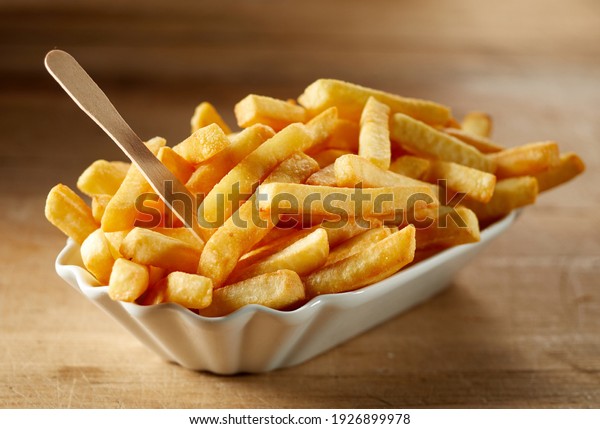 Tasty deep fried potato slices\
with organic fork in ceramic bowl on wooden table in\
sunlight