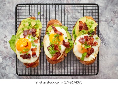 Tasty delicious homemade toasts with fried egg, bacon, avocado, lettuce and chive. Served on black grill - Powered by Shutterstock