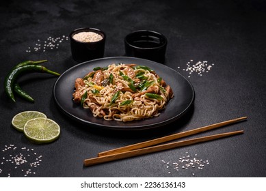 Tasty dish of Asian cuisine with rice noodles, chicken, asparagus, pepper, sesame seeds and soy sauce on dark concrete background