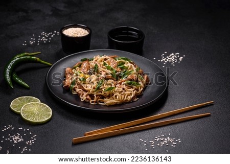 Tasty dish of Asian cuisine with rice noodles, chicken, asparagus, pepper, sesame seeds and soy sauce on dark concrete background