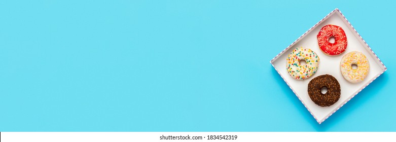 Tasty donuts in a box on a blue background. Concept of sweets, bakery, pastries, coffee shop. Banner. Flat lay, top view