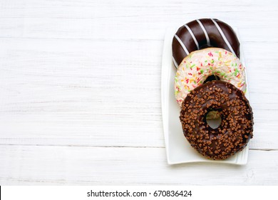 Tasty donuts with icing and chocolate on white wooden background, copy space