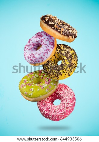 Tasty doughnuts in motion falling on pastel blue background, close-up.