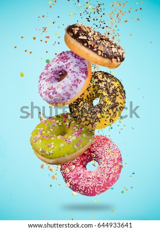 Tasty doughnuts in motion falling on pastel blue background, close-up.