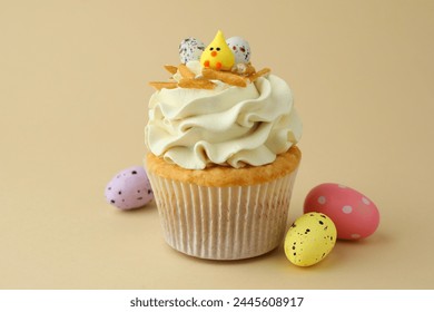 Tasty Easter cupcake with vanilla cream and candies on beige background