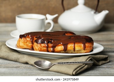 Tasty eclairs and cup of tea on wooden table