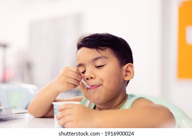 Tasty food and Delicious food concept.Portrait asian boy with spoon eat yogurt cup with milk pudding into mouth.Handsome male child boy is showing delicious.Tasty face hungry kid.boy child happy meal.