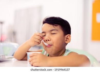 Tasty Food And Delicious Food Concept.Portrait Asian Boy With Spoon Eat Yogurt Cup With Milk Pudding Into Mouth.Handsome Male Child Boy Is Showing Delicious.Tasty Face Hungry Kid.boy Child Happy Meal.