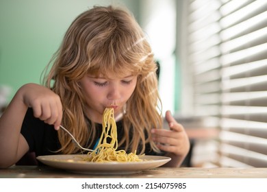 Tasty Food, Messy Child Eating Spaghetti Happy Child Boy With Spoon Eats Itself. Kid Eating Food On Kitchen. Close Up Portrait Of Funny Kid Eating Noodles Pasta.