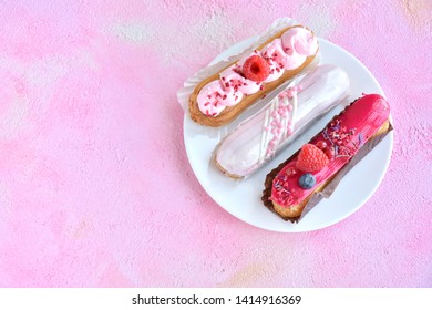 Tasty French eclairs cake with creative pink decor and fresh berries on pink textured table. Selective focus. Delicious dessert profiteroles with pink and red icing and sugar decor elements. 