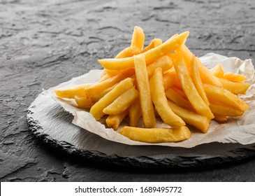 Tasty french fries potatoes on paper over black stone background. Hot fast food, close up