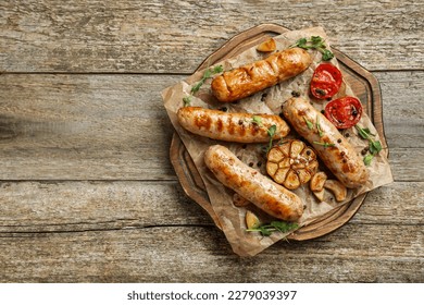 Tasty fresh grilled sausages with vegetables on wooden table, top view. Space for text